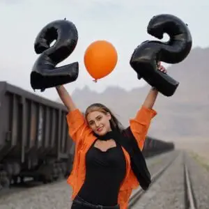 A Woman Holding Black Inflatable Number Balloons Standing on Railroad Track